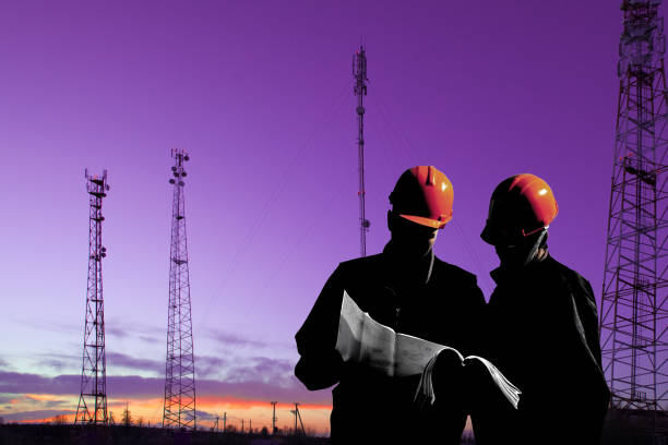 Silhouette of professional industrial climber in helmet and uniform works at height for instaling communication equipment and antenna and telecommunication towers with sunset sky as background. Risky extreme job. Industrial climbing.Industrial climbing background at construction site